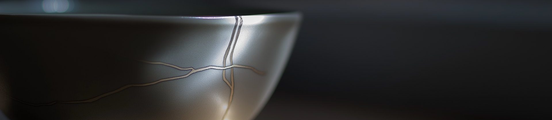 A gray ceramic bowl in soft light, its cracks mended with kintsugi seams
